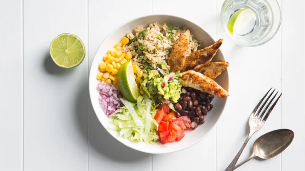 A bowl filled with rice, beans, corn, diced tomatoes, and a wedge of lime, showcasing a colorful and nutritious meal