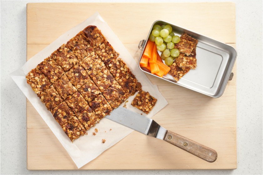 A cutting board displaying a portion of granola accompanied by assorted fruits