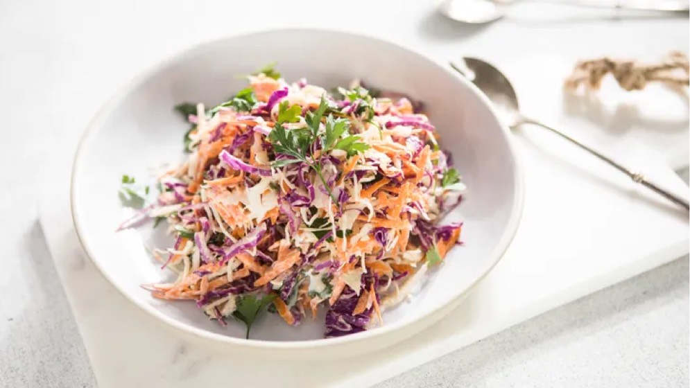 A bowl of coleslaw featuring shredded cabbage, carrots, and garnished with fresh parsley